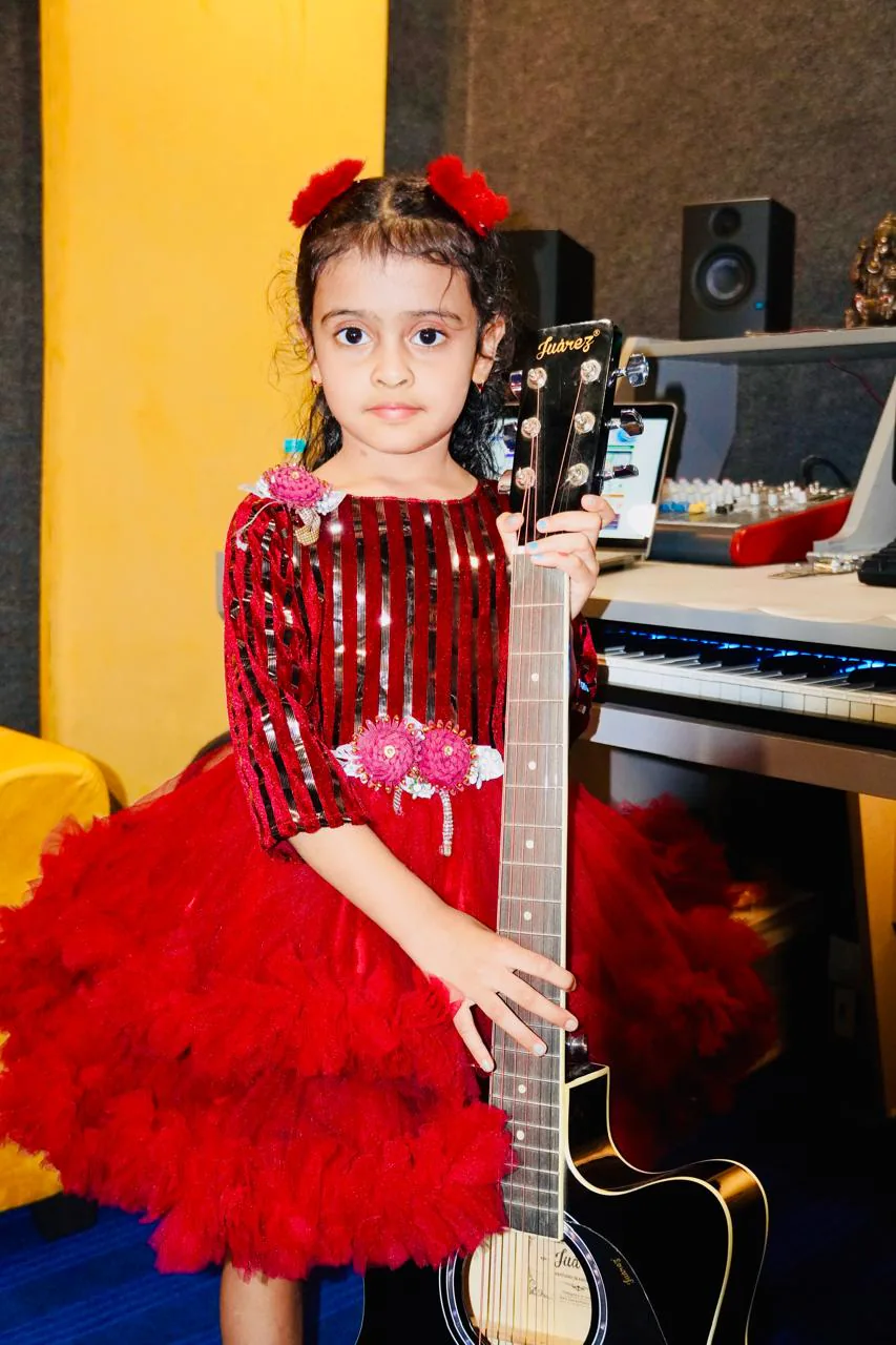 Young student holding a guitar beside the production desk